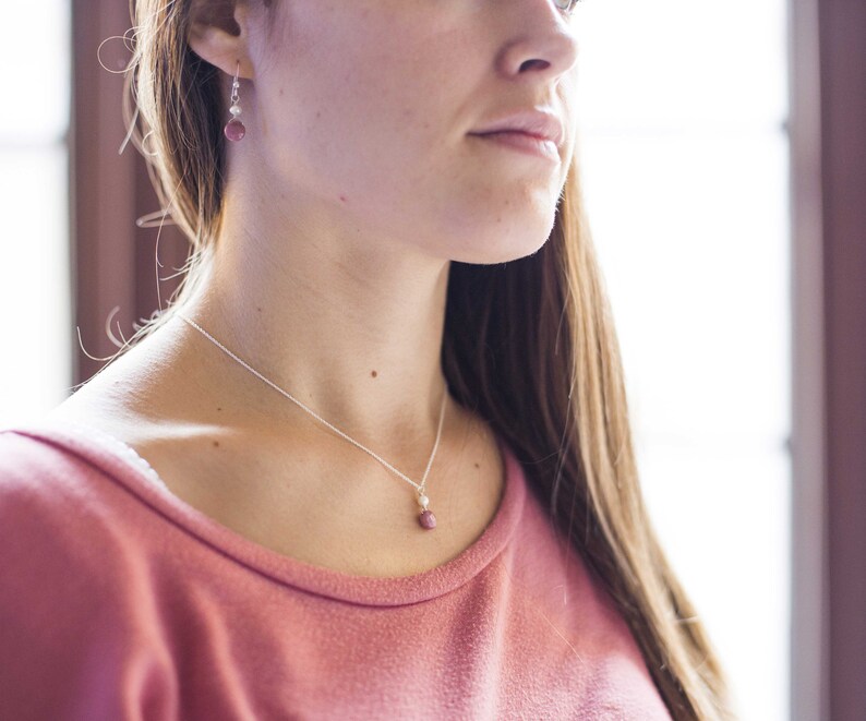 Puede incluir: Una mujer con un su&eacute;ter rosa con un collar de cadena plateada y un peque&ntilde;o colgante de piedra rosa. Tambi&eacute;n lleva pendientes plateados con una peque&ntilde;a piedra rosa.