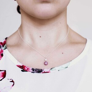 Puede incluir: Un collar de cadena de plata con un peque&ntilde;o colgante de piedra rosa y un acento de perla blanca.