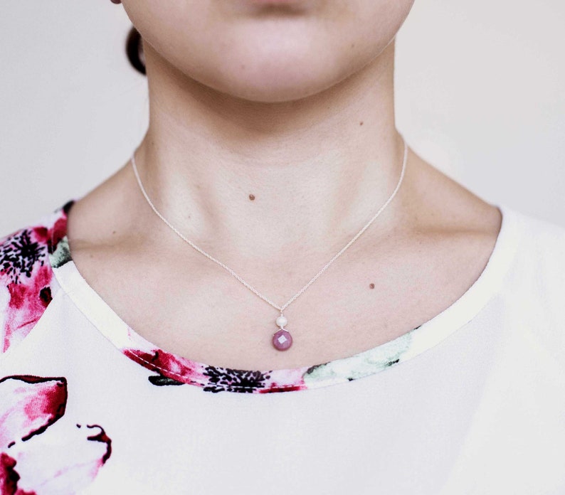 Puede incluir: Un collar de cadena de plata con un peque&ntilde;o colgante de piedra rosa y un acento de perla blanca.