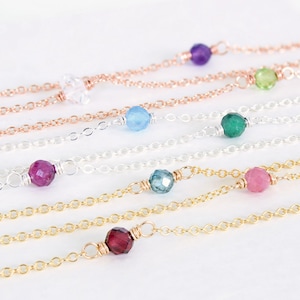 May include: A set of delicate necklaces with various gemstone beads, including clear, blue, green, pink, and red. Each necklace features a different colored gemstone bead.