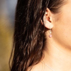 Puede incluir: Un par de pendientes de plata con una piedra preciosa rosa y una peque&ntilde;a perla colgante. Los pendientes los lleva una persona con el pelo largo y casta&ntilde;o.