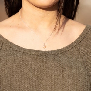 May include: A close-up of a woman wearing a green waffle knit sweater with a delicate silver chain necklace featuring a small pearl pendant.