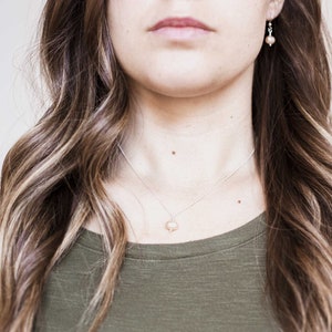May include: A woman with long brown hair wearing a green shirt and a silver necklace with a pearl pendant. She is also wearing small pearl earrings.