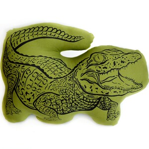 May include: A green pillow shaped like an alligator with a black outline. The alligator's mouth is open and its teeth are visible.