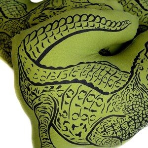 May include: Three green fabric alligator pillows with black alligator print designs. The pillows are shaped like alligators and have a textured fabric.