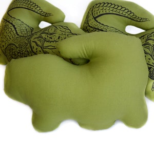 May include: Three green plush alligator pillows with black alligator designs. The pillows are shaped like alligators and have a soft, plush texture.