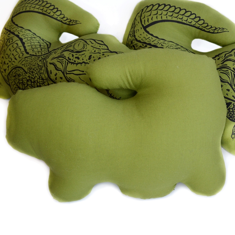 May include: Three green plush alligator pillows with black alligator designs. The pillows are shaped like alligators and have a soft, plush texture.