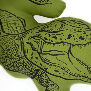 May include: Green pillow with a black and white illustration of an alligator with its mouth open. The alligator is facing the right side of the image.