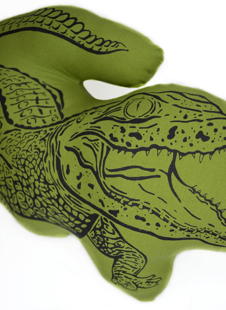 May include: Green pillow with a black and white illustration of an alligator with its mouth open. The alligator is facing the right side of the image.