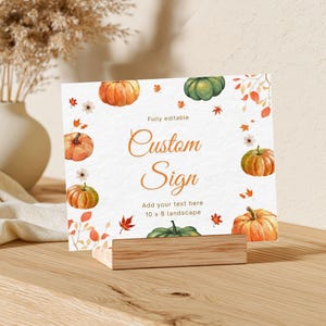 Puede incluir: Un letrero rectangular horizontal con un borde de acuarela de calabazas y hojas de otoño. El texto dice Fully editable Custom Sign Add your text here 10 x 8 landscape. El letrero se exhibe en un soporte de madera clara sobre una superficie.