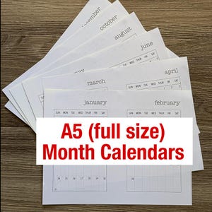 May include: A stack of white paper sheets featuring printed monthly calendar grids for January through December. Each sheet displays the month name in a typewriter-style font above a grid with days of the week and numbered dates. Text reads A5 (full size) Month Calendars.