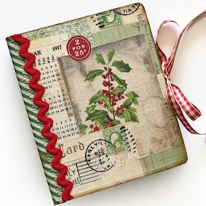 Puede incluir: Un pequeño diario hecho a mano con una cubierta de tela roja y verde. La cubierta presenta una ilustración vintage de bayas de acebo y un sello rojo que dice "2 por 25c". El diario está atado con una cinta de cuadros rojos y blancos.