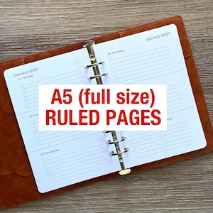 May include: An open A5 planner with a brown leather-effect cover and a silver metal ring binder mechanism. The white paper pages feature a weekly layout for January 2027 with ruled lines and checkboxes. Text on the page reads A5 (full size) RULED PAGES.