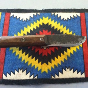 May include: A small, rusty knife with a wooden handle. The knife is lying on a colorful fabric with a geometric pattern.