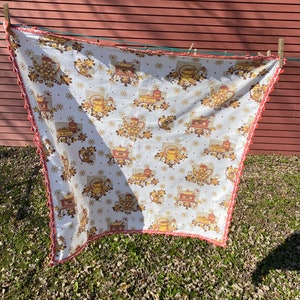 May include: A white tablecloth with a red and white crocheted border. The tablecloth features a repeating pattern of brown teapots, flowers, and stars.
