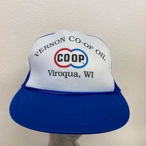 May include: A white trucker hat with a blue mesh back. The hat has a red, white, and blue logo that says "CO-OP" and the text "Vernon Co-op Oil Viroqua, WI".