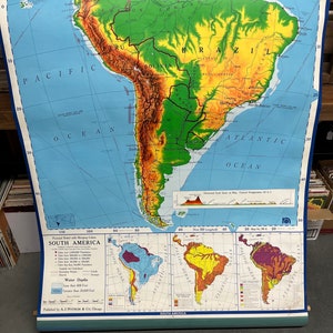 May include: A vintage educational map of South America with a pictorial relief with merging colors. The map shows the continent's physical features, including mountains, rivers, and coastlines. The map also includes a key with information about population density, land utilization, and water depths. The map is titled "South America" and is published by A.J. Nystrom & Co., Chicago.