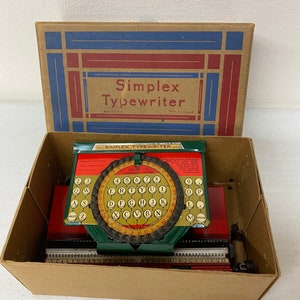 May include: A vintage green and red toy typewriter in its original box. The box is brown with blue and red accents and the text "Simplex Typewriter" printed on the top. The typewriter has a green body with a red base and a red paper roller. The keyboard is green with white keys and the text "SPECIAL AIR KEYBOARD MODEL" printed on the top.