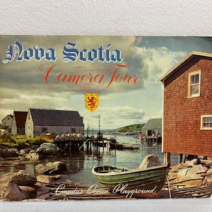 May include: A vintage postcard featuring a colorful image of a quaint seaside village in Nova Scotia, Canada. The postcard reads "Nova Scotia Camera Tour" and "Canada's Ocean Playground".