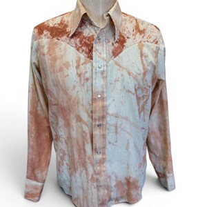 May include: A long-sleeve button-down shirt featuring a cream base color with an irregular, mottled rust-colored pattern. The shirt includes a pointed collar, a front button placket with metallic buttons, and quilted detailing across the shoulder yoke.