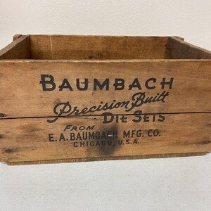 May include: A wooden crate with the text "Baumbach Precision Built Die Sets From E.A. Baumbach Mfg. Co. Chicago, U.S.A."