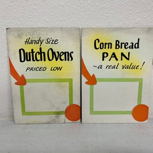 May include: Two vintage advertising signs for kitchenware. The left sign advertises "Handy Size Dutch Ovens" with the text "Priced Low" and an orange arrow pointing to a green rectangle. The right sign advertises "Corn Bread PAN - a real value!" with an orange arrow pointing to a green rectangle.