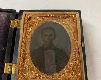 May include: A black and gold framed photograph of a man in a suit and bow tie. The photo is in a wooden case with a velvet lining.