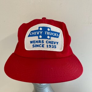 May include: Red trucker hat with a white patch that says "Chevy Trucks Wehrs Chevy Since 1935" in blue lettering.