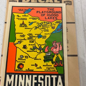 May include: A vintage decal of a map of Minnesota, featuring the text "The Playground of 10,000 Lakes". The map is illustrated with a cartoon lumberjack holding an axe, and various cities and landmarks are labeled.