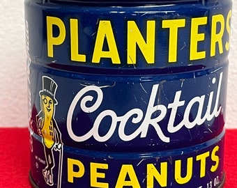 May include: A blue metal can with a white lid. The can has a yellow label with the text "PLANTERS Cocktail PEANUTS" and a cartoon image of Mr. Peanut. The label also includes the text "NET WT. 13 OZ."