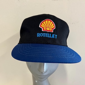 May include: A black and blue baseball cap with a yellow and red shell logo and the text "ROTELLAT" embroidered on the front.