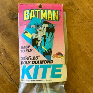 May include: A blue and yellow Batman kite with a 30 1/2 inch by 25 inch poly diamond design. The kite is packaged in a plastic bag with a cardboard header featuring a cartoon image of Batman. The header also includes the text "Easy to Fly" and "Ages: 7 to adult, Wind Rated: 5 to 12 m.p.h."