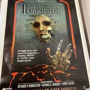 May include: A vintage movie poster for "Tales from the Darkside" volume 6. The poster features a creepy, decaying face with a skull-like jaw and a hand reaching out from the ground. The text on the poster reads "Tales from the Darkside" and "Vol. 6".