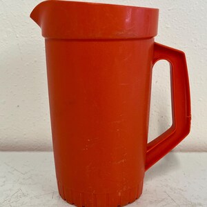May include: A bright orange plastic jug with a handle. The jug has a textured base.