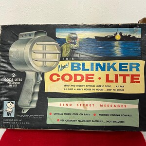 May include: A vintage box for a Navy Blinker Code Lite toy. The box features a black and white illustration of a ship at sea and a close-up of the toy, which is a silver flashlight with a black handle. The box also includes the text "Navy Blinker Code Lite" and "Send Secret Messages".