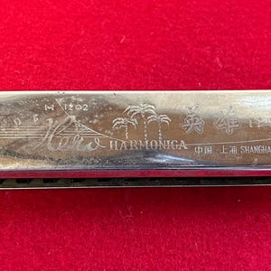 May include: A silver harmonica with the text "Hohner & Harmonica" and "Shanghai, China" engraved on the front. The harmonica has a silver finish and a black plastic comb.