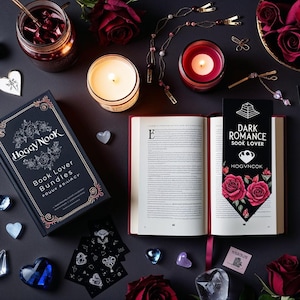 Pode incluir: Uma vista aérea de uma cena estética escura com um livro, velas e rosas. O livro aberto tem um marcador que diz "Dark Romance Book Lover". Outros itens incluem um pote de geleia, cristais decorativos e um livro intitulado "Hoggy Nook Book Lover Bundles."