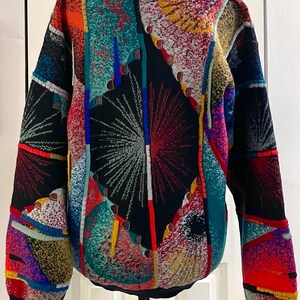 Puede incluir: Un su&eacute;ter estampado y colorido con un dise&ntilde;o &uacute;nico. El su&eacute;ter presenta un mosaico de colores vibrantes que incluyen rojo, azul, amarillo y verde. El dise&ntilde;o incluye formas geom&eacute;tricas y patrones abstractos, con un fondo negro y pu&ntilde;os negros.
