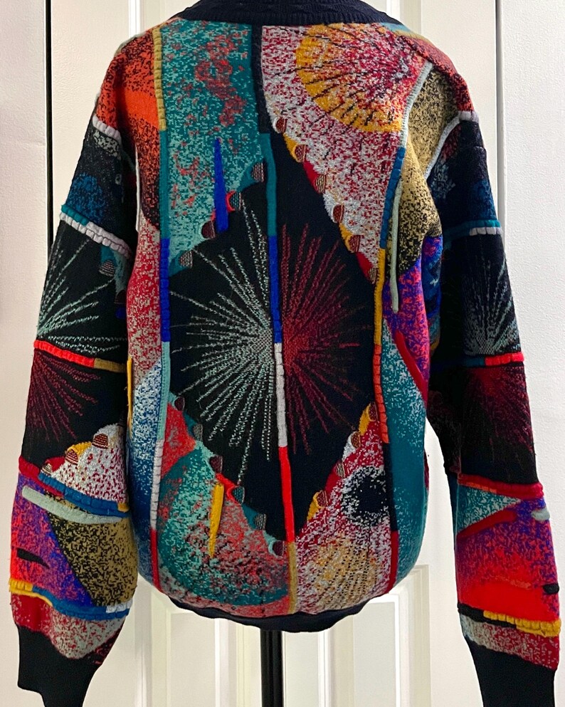 Puede incluir: Un su&eacute;ter estampado y colorido con un dise&ntilde;o &uacute;nico. El su&eacute;ter presenta un mosaico de colores vibrantes que incluyen rojo, azul, amarillo y verde. El dise&ntilde;o incluye formas geom&eacute;tricas y patrones abstractos, con un fondo negro y pu&ntilde;os negros.