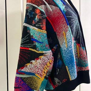 Puede incluir: Un c&aacute;rdigan estampado y colorido con base negra. El dise&ntilde;o incorpora formas geom&eacute;tricas y patrones abstractos en rojo, azul, naranja y turquesa. El c&aacute;rdigan tiene cuello en V y mangas largas.