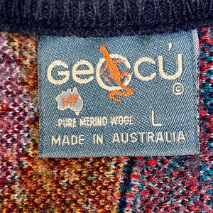 Puede incluir: Primer plano de una etiqueta azul con la marca "geccu" y un logotipo de canguro, cosida a una prenda de lana colorida. La etiqueta dice "PURE MERINO WOOL" y "MADE IN AUSTRALIA". La prenda es una mezcla de rojo, amarillo y azul.