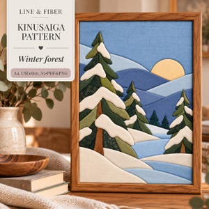 May include: A framed Kinusaiga pattern art piece titled Winter forest, featuring fabric-covered layers depicting snow-covered evergreen trees, rolling blue hills, and a yellow sun. The text reads LINE & FIBER KINUSAIGA PATTERN Winter forest.