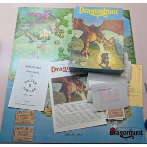 May include: A vintage board game titled "Dragonhunt" with a box featuring a dragon illustration. The game includes a map, cards, dice, and instruction booklets. The box reads "Avalon Hill Announces Its Silver Jubilee 1958-1983".
