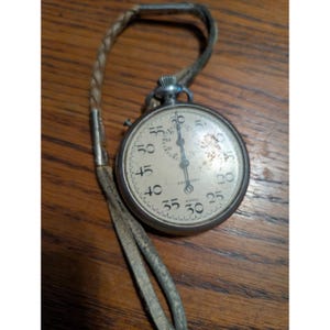 May include: A vintage stopwatch with a silver case and a cream-coloured face. The watch has black numerals and hands, and a leather strap. The word "SECURITY" is printed on the face, along with "SWISS".