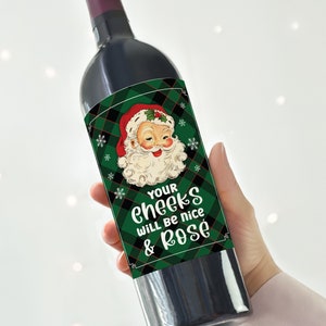 May include: A green and black plaid wine bottle label with a cartoon image of Santa Claus. The text on the label reads "Your cheeks will be nice & rose".