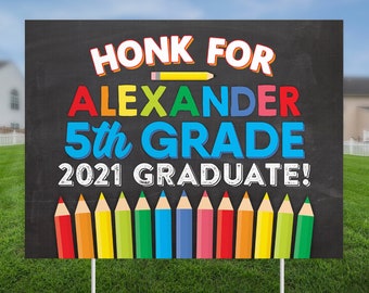 May include: A black chalkboard sign with the text "Honk for Alexander 5th Grade 2021 Graduate!" in colorful letters. A yellow pencil is drawn above the name. A row of colorful pencils are drawn at the bottom of the sign.