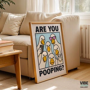 May include: A framed art print featuring a cartoon illustration of several white ducks. The ducks are depicted with various expressions and accessories, including sunglasses and a smartphone. The text "ARE YOU POOPING?" is displayed.
