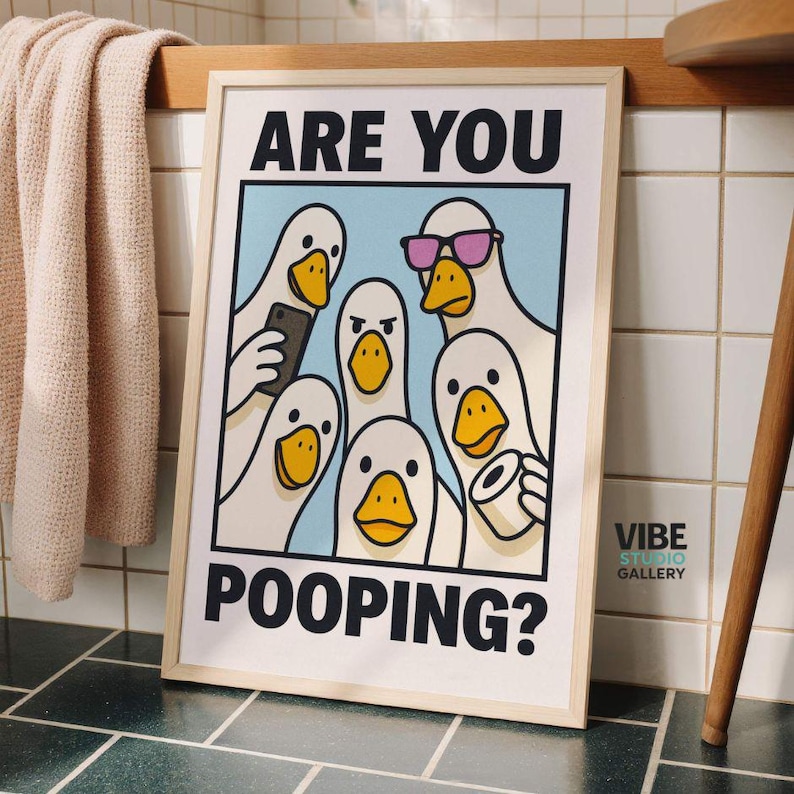 May include: A framed art print featuring a cartoon illustration of several white geese with yellow beaks. The geese are depicted in a bathroom setting, with the text "ARE YOU POOPING?" at the top and bottom.