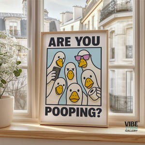 May include: Framed art print featuring a group of cartoon ducks with the text "ARE YOU POOPING?". The ducks are white with yellow beaks, some holding a phone, toilet paper, and wearing sunglasses. The art is displayed on a windowsill.