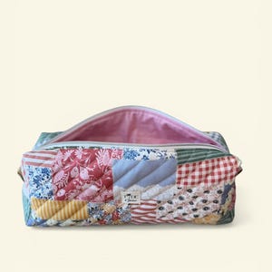 May include: A patchwork fabric cosmetic bag with a zipper closure. The bag features a variety of patterned fabrics in red, blue, yellow, and white. The interior is lined with pink fabric. The bag has a label that reads "Tide & Thrive".